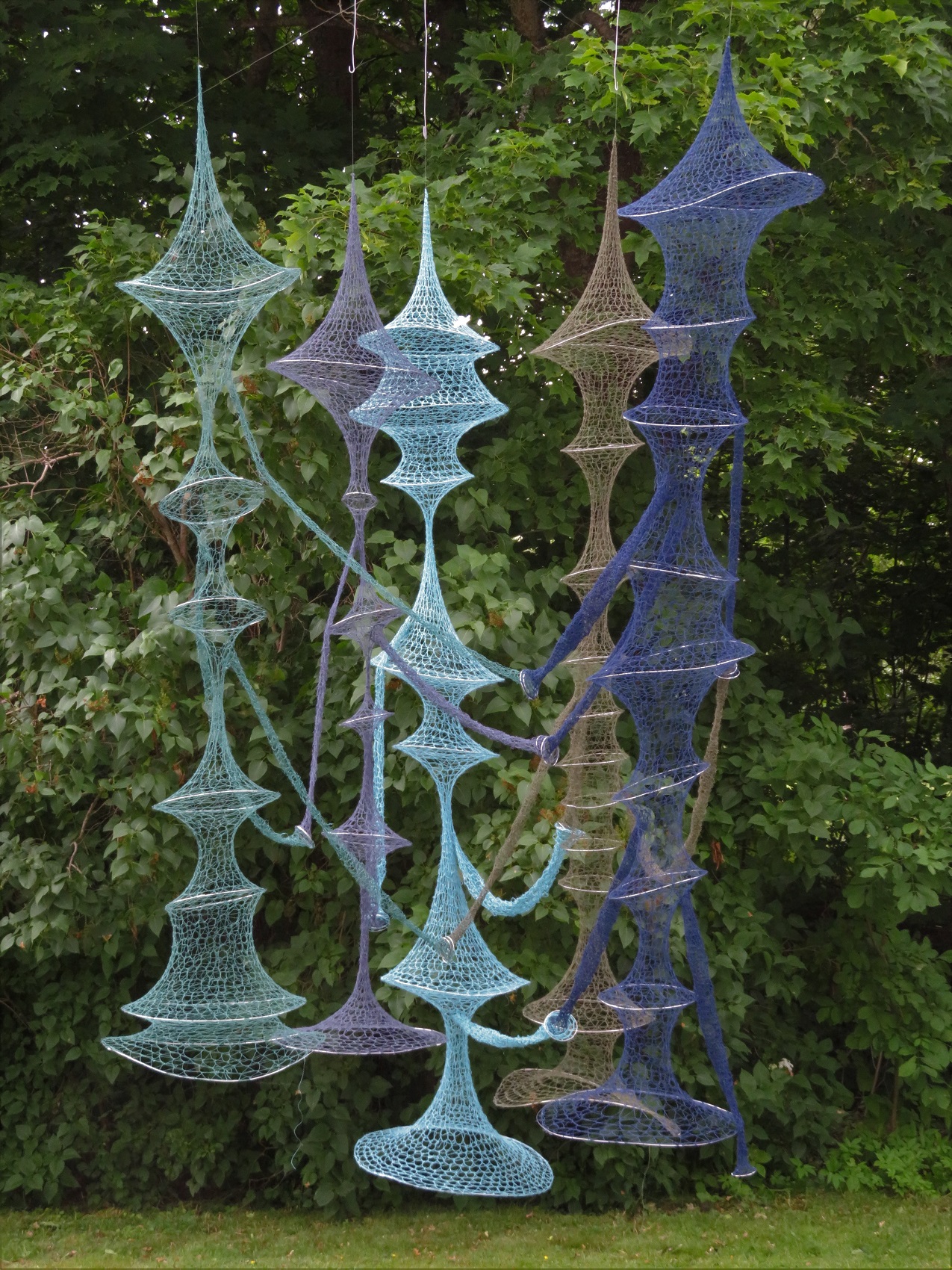 Fotografi av skulptur med flera virkade, hängande former i blått och turkos garn.