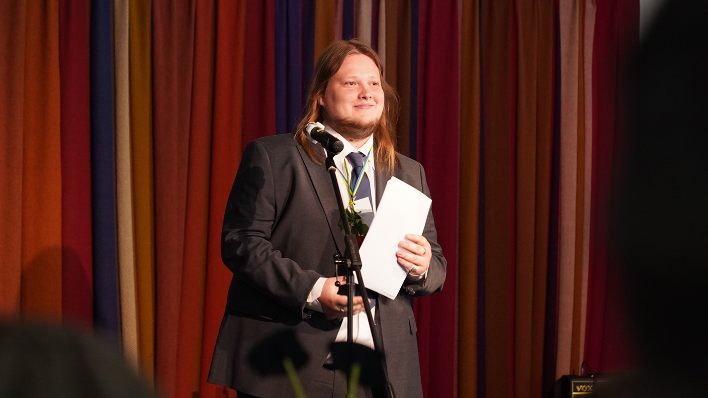 En man står framför en mikrofon med ett papper i handen.
