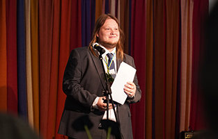 En man står framför en mikrofon med ett papper i handen.