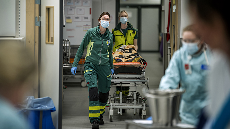 Två ambulans sjuksköterskor rullar in en patient på en bår.