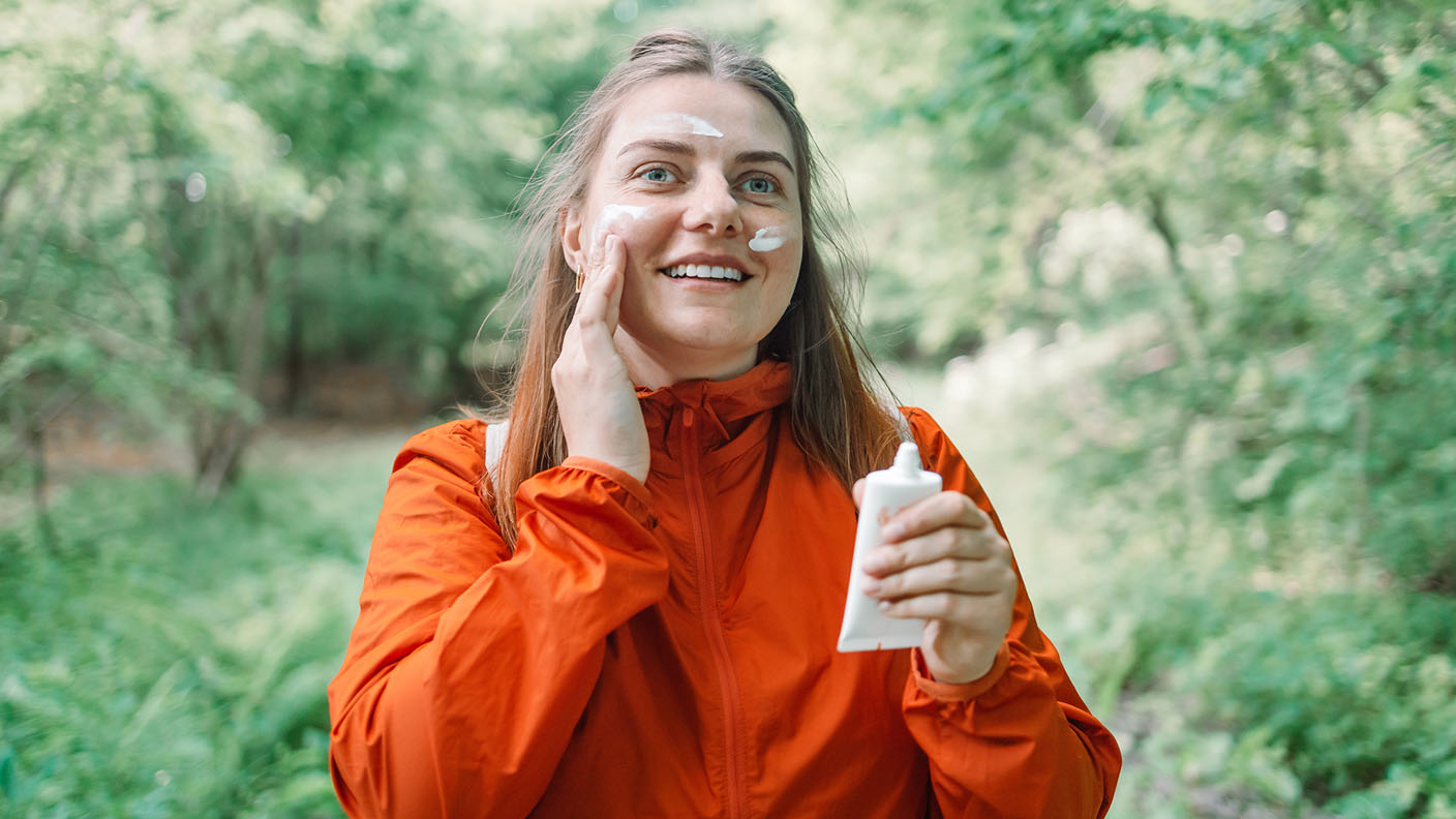 Kvinna som smörjer sig med solskyddskräm i ansiktet