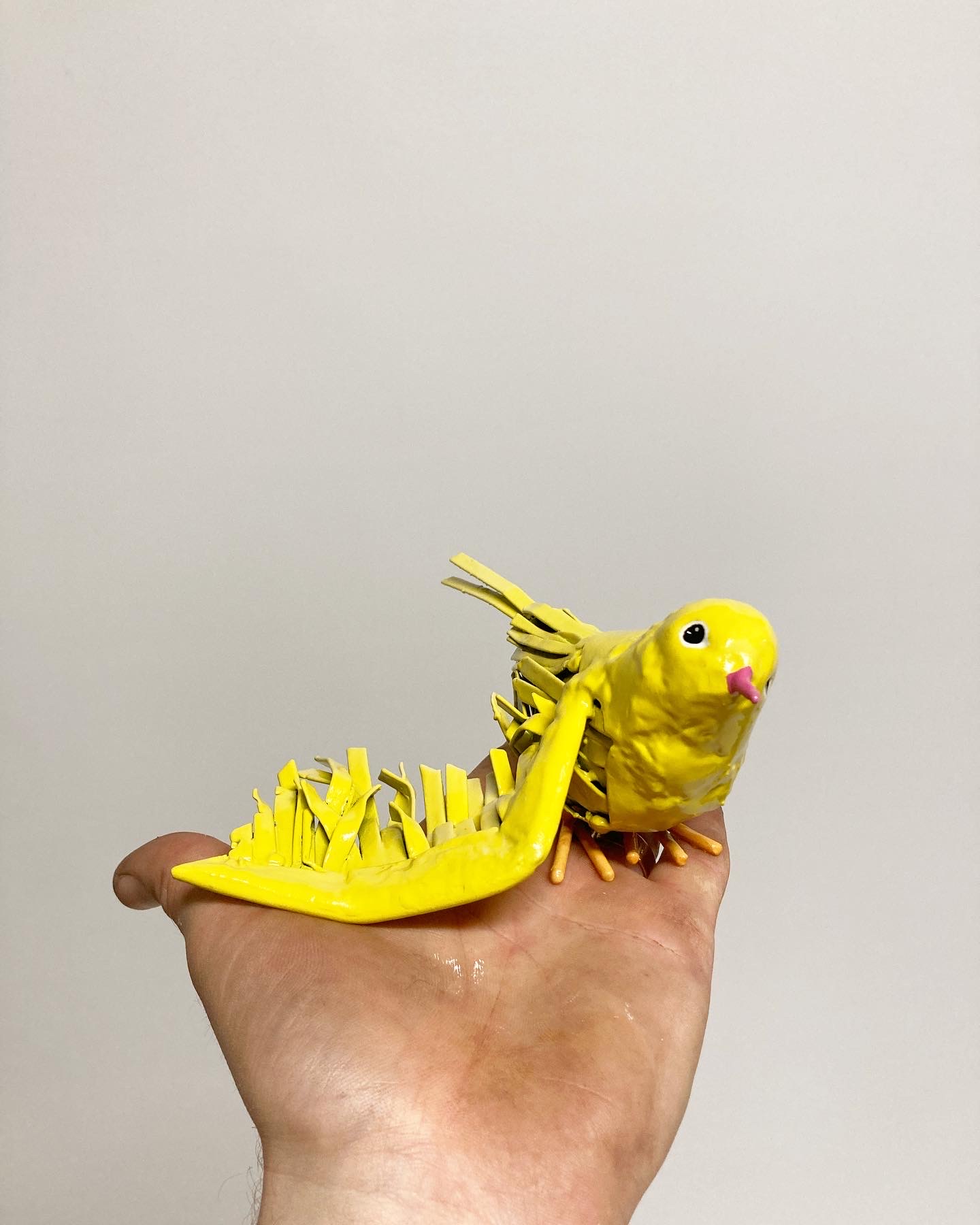 Fotografi av hand som håller liten skulptur av en gul fågel.