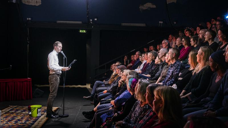 På bild: Michael Horvath Dahlman. Klubb Bubbla på Nya China. 8 novmber 2022. Poesi kan vara brevet du skrev men aldrig skickade till din hemliga kärlek i skolan, eller ett språkmaterialistiskt experiment om E-nummer i mat. Det kan vara kopierat i smyg på jobbet eller tryckt i böcker av landets största förlag. Det kan vara skrivet av en professor, eller uppdiktat av en tvååring som sitter uttråkad i en kundvagn och leker med förbipasserande ord. Det kan huggas i sten eller ropas ut över ett torg och försvinna.Klubb Bubbla ställer allt detta på samma scen, och ställer inte det ena ovanför det andra. Därför är det estradpoesins vardagsrum. Här ser du vinnare från Poetry Slam-SM, debutanter från bokförlagen, och kanske någon från ditt kvarter