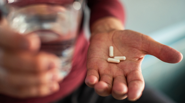 En man håller tre piller i ena handen och ett vattenglas i de andra.