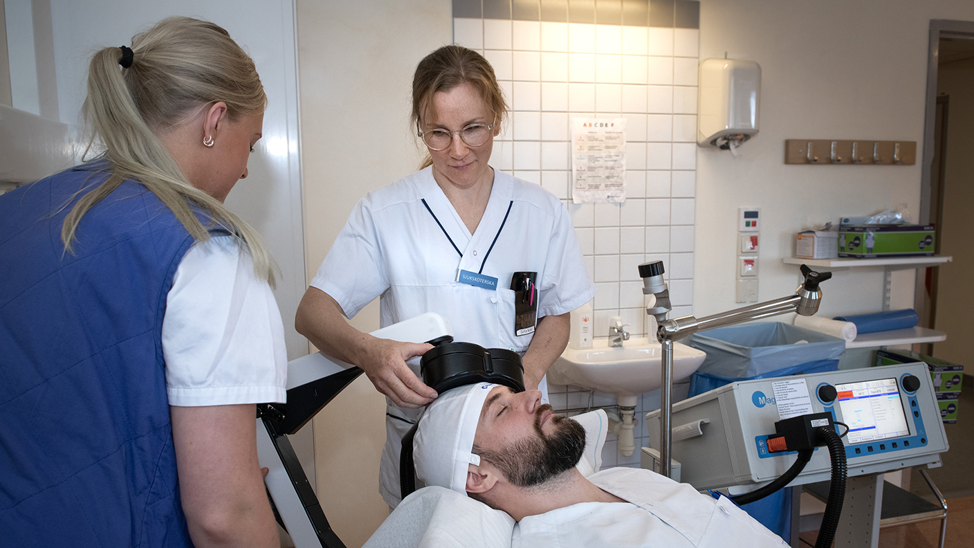 Två sjuksköterskor ger en patient som ligger ner på en brits magnetstimulering.