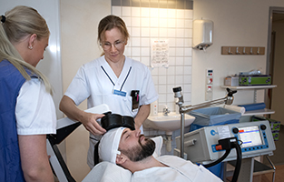 Två sjuksköterskor ger en patient som ligger ner på en brits magnetstimulering.