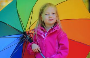 Liten flicka håller i ett regnbågsfärgat paraply