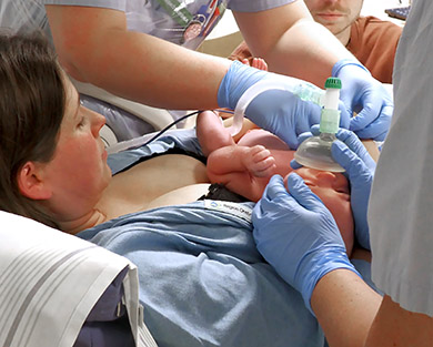 Sjukvårdspersonal hjälper det nyfödda barnet som ligger på mammans bröst.