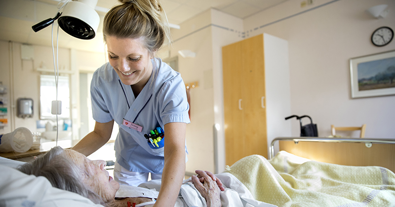 Sjuksköterska hjälper patient i säng