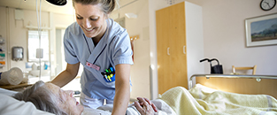Sjuksköterska hjälper patient i sän