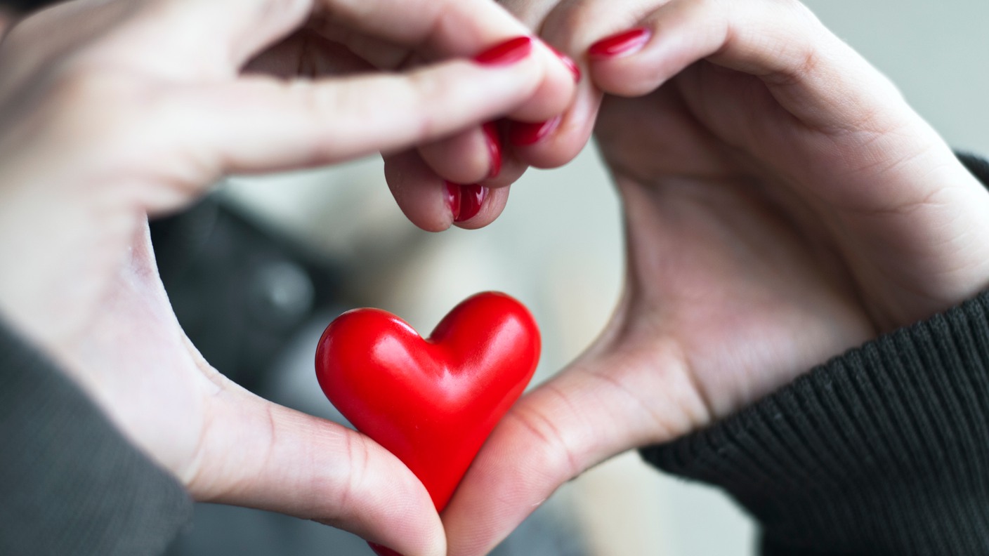 Händer bildar ett hjärta runt ett rött hjärta.