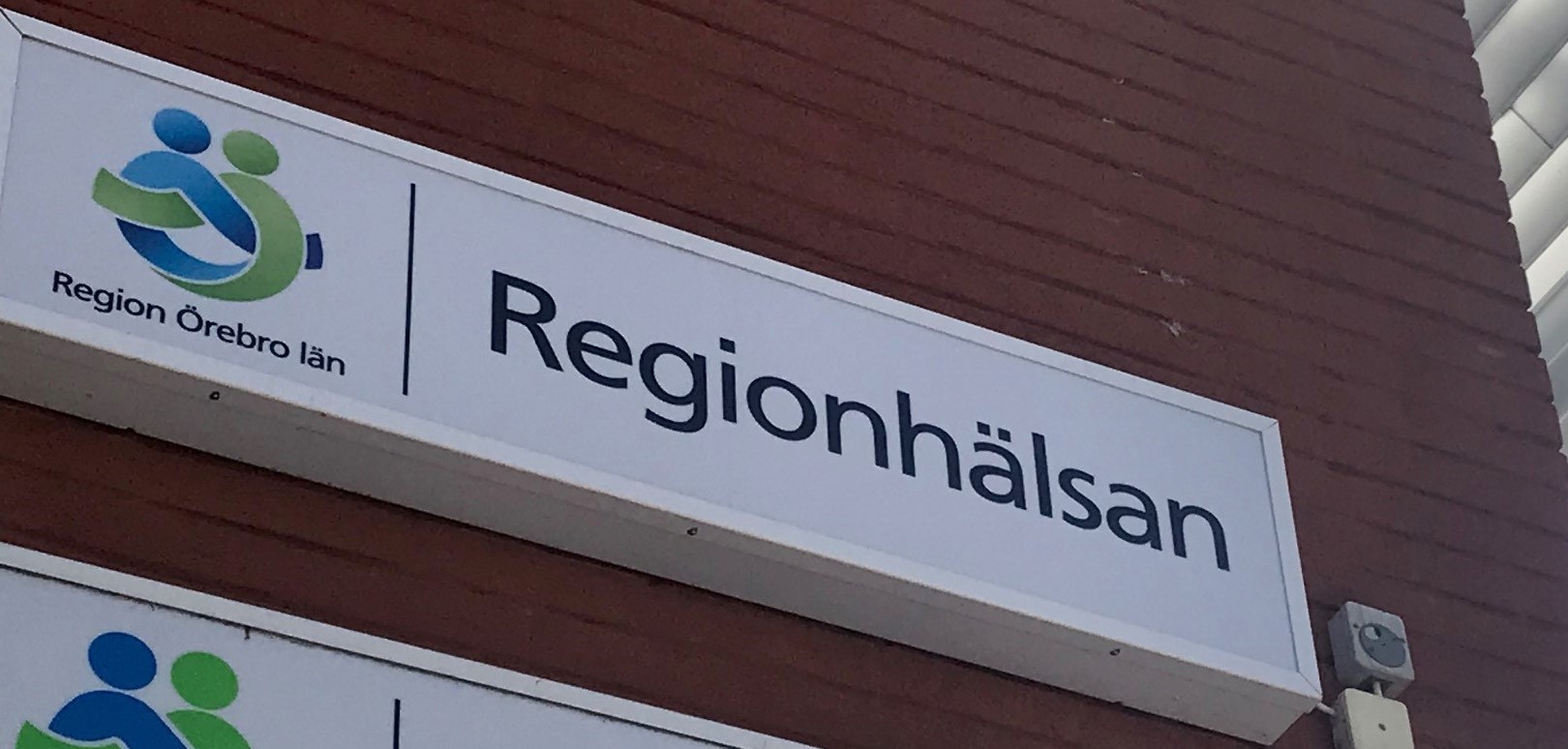 Fasadskylt i form av Regionhälsans logotyp på tegelvägg 