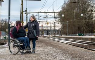 Två personer på en perrong. En person sitter i rullstol och en står bredvid.
