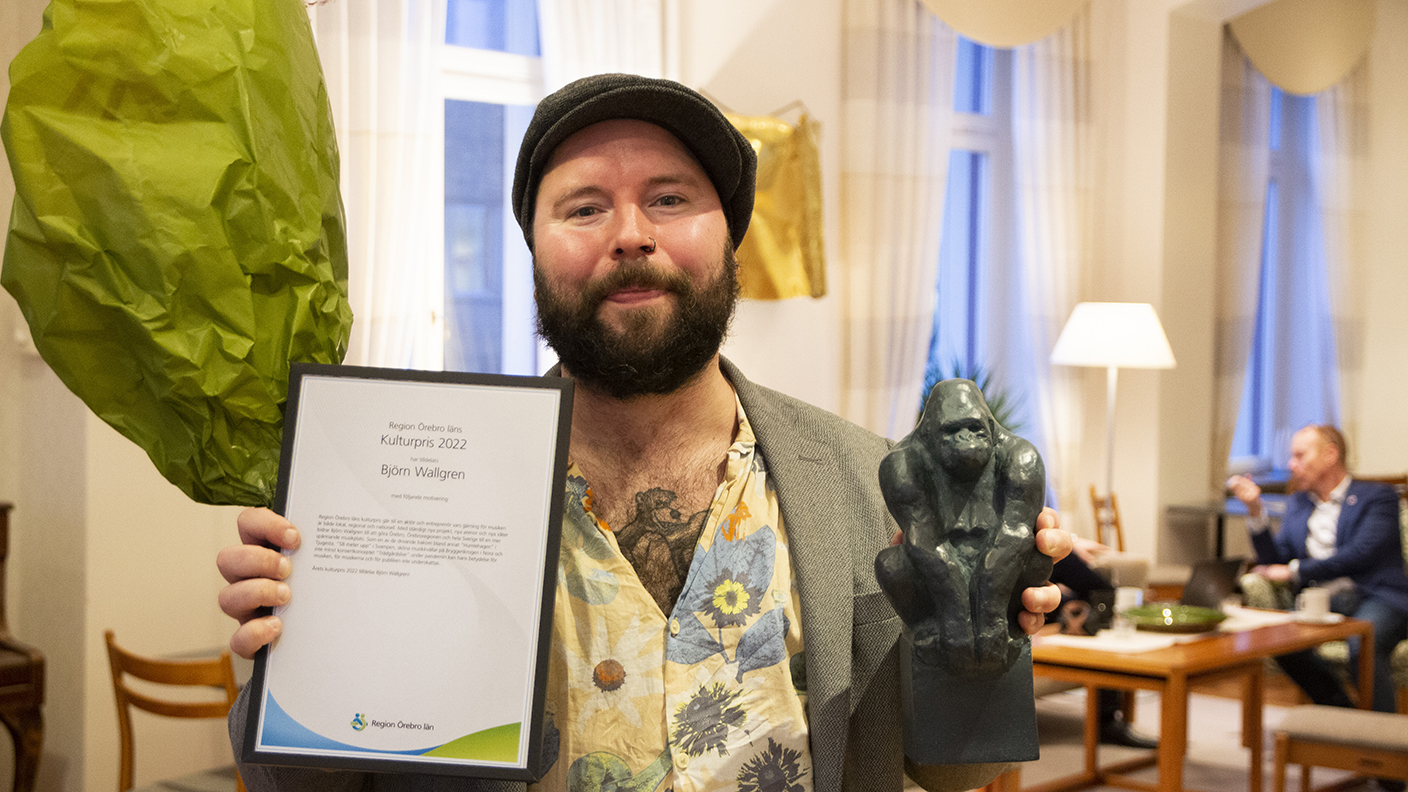 Person tar emot Region Örebro läns kulturpris - blommor, statyett och diplom.