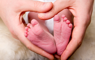 Händer bildar ett hjärta runt en nyfödds fötter.