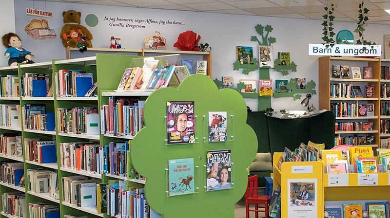 Barnhörnan på patientbiblioteket USÖ. Gröna och gula hyllor med böcker.  Vimplar i taket. 