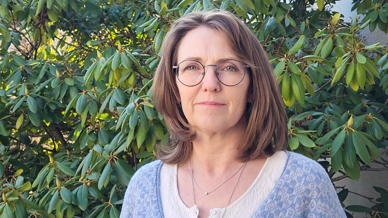 En kvinna står framför en rhododenronbruske.