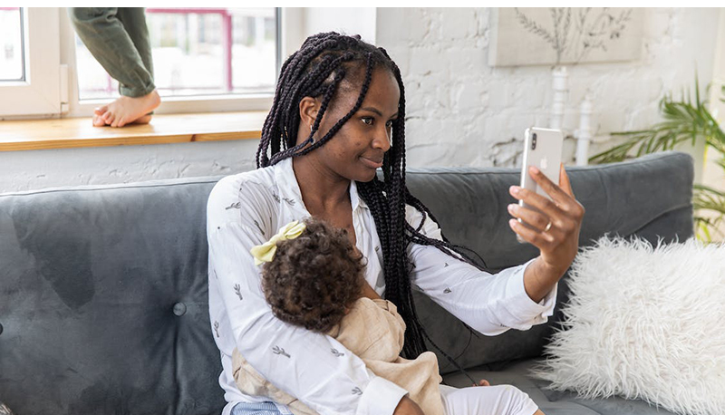 Ung mörkhyad kvinna med ett litet barn i famnen har kontakt med vården via sin mobiltelefon