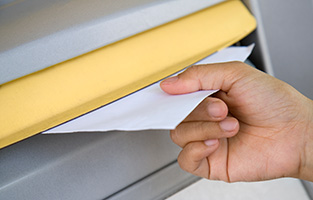 Hand som lägger ett brev i en brevlåda. 