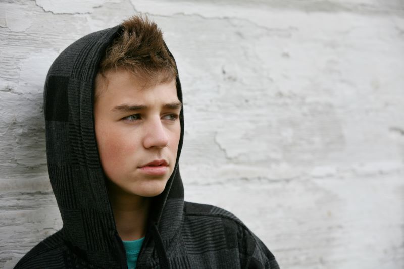 En ung kille som tittar bort, han har en svart hoodie med luvan uppdragen över huvudet, han ser allvarlig ut 