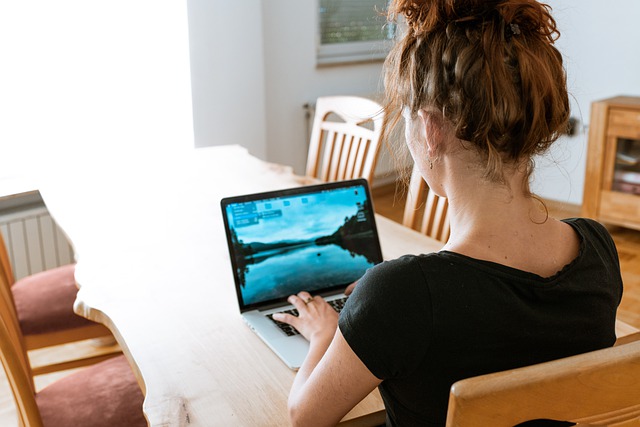 En kvinna sitter vid ett matbord och arbetar vid en laptop. Vi ser henne bakifrån.