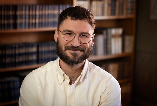 Mörkhårig man med skägg och runda glasögon som ler