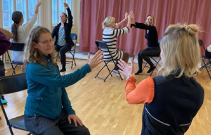 Personer sitter mitt emot varandra på stolar och gör spegeldans