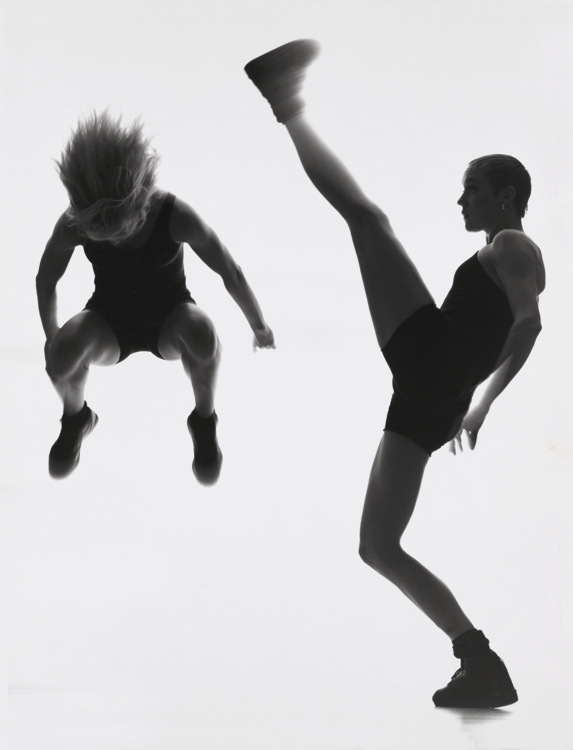 Två dansare in action - en i jämfotahopp och en sträcker upp ena benet ovanför huvudet
