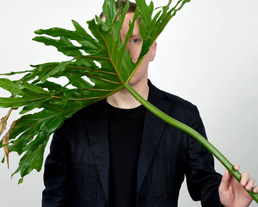 James Webb kikar fram bakom ett blad av en stor grön växt som han håller i handen