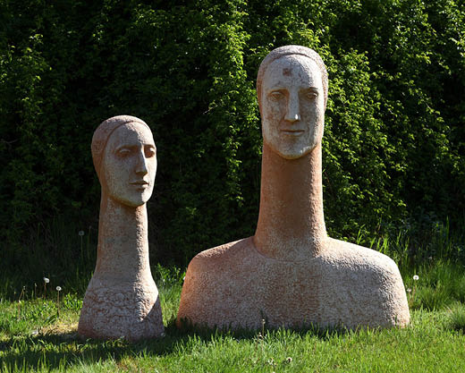 Två torso-skulpturer med långa halsar på gräsmatta