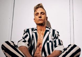 Axel Schylström, i svart vitrandig kostym sitter med benen i kors på ett schackrutigt golv. Under kavajen anas hans brännskadade hud.