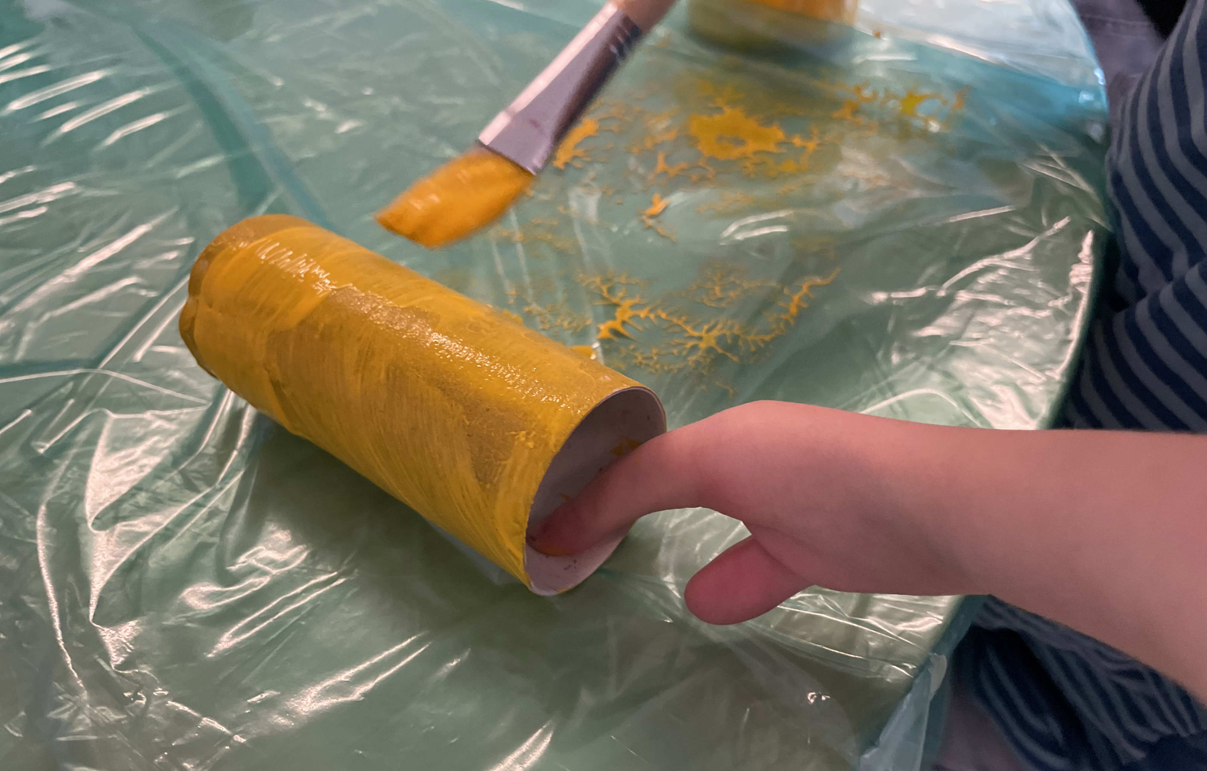 Barnhand med dysmeli som målar en toarulle gul